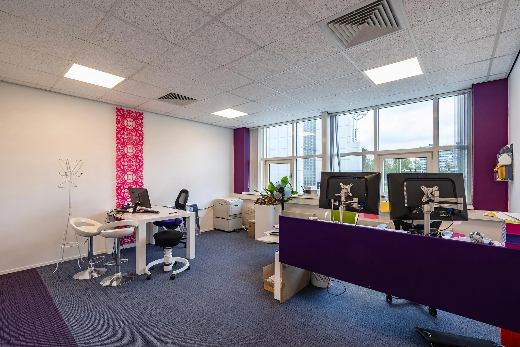 Modern kantoorinterieur in het Rhijnspoor-gebouw met werkplekken, paarse accenten en grote ramen.