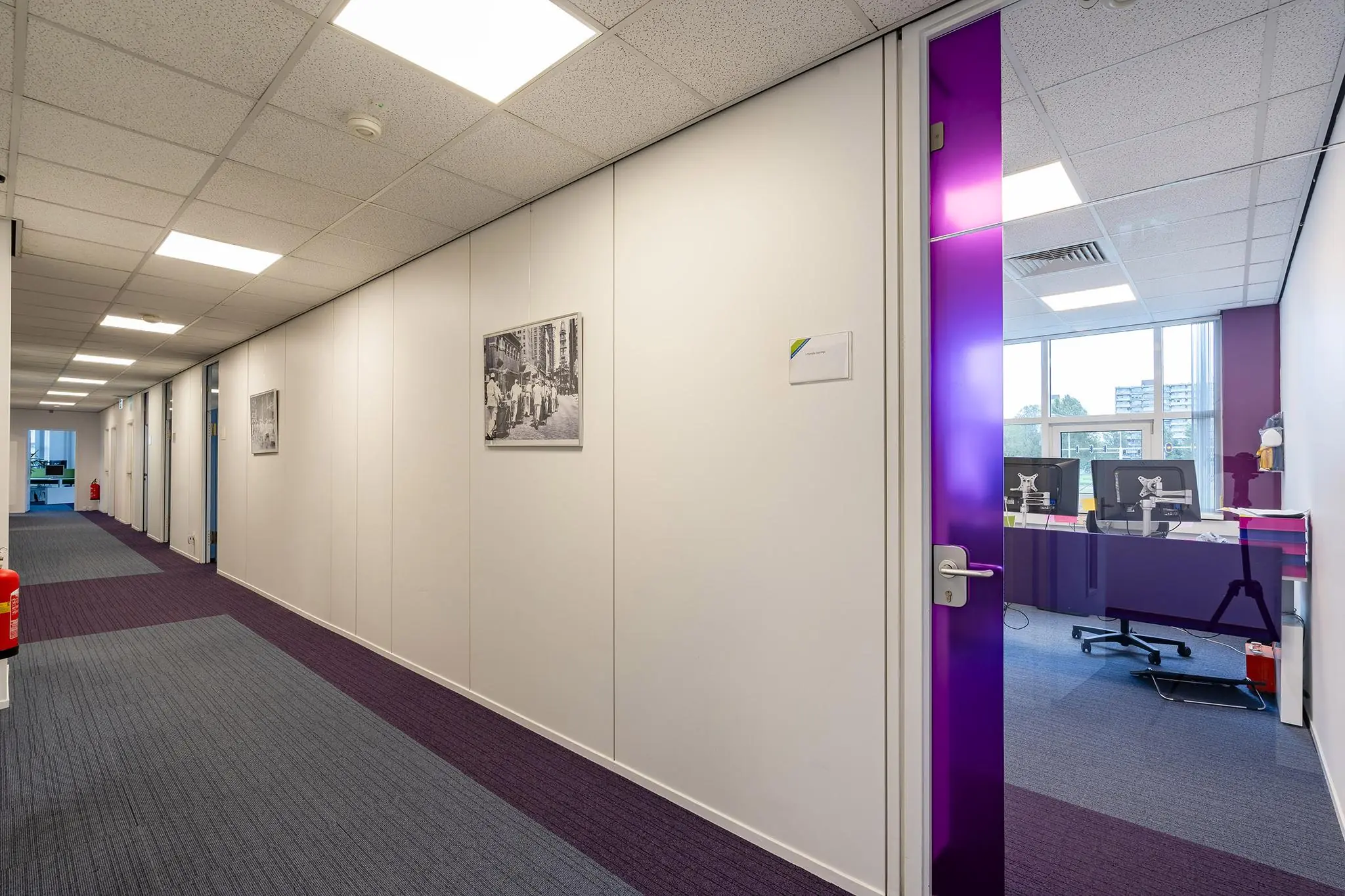 Moderne kantoorruimte in het Rhijnspoorgebouw met paarse accenten en zicht op werkplekken door glazen deur.