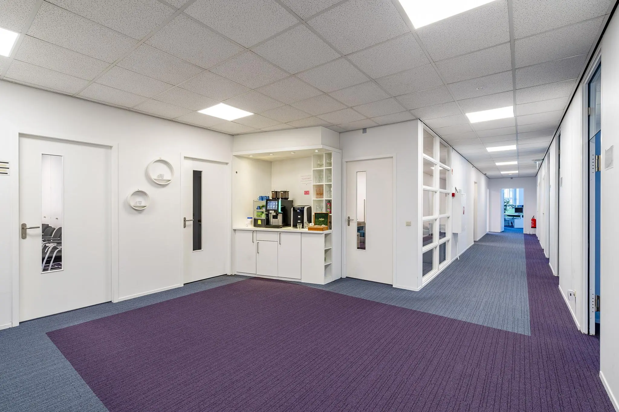 Modern kantoorinterieur met een koffiehoek en paarse vloerbedekking in het Rhijnspoorgebouw.