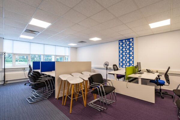 Moderne open kantoorruimte aan het Rhijnspoor met bureaus, bureaustoelen, gestapelde stoelen en hoge krukken.