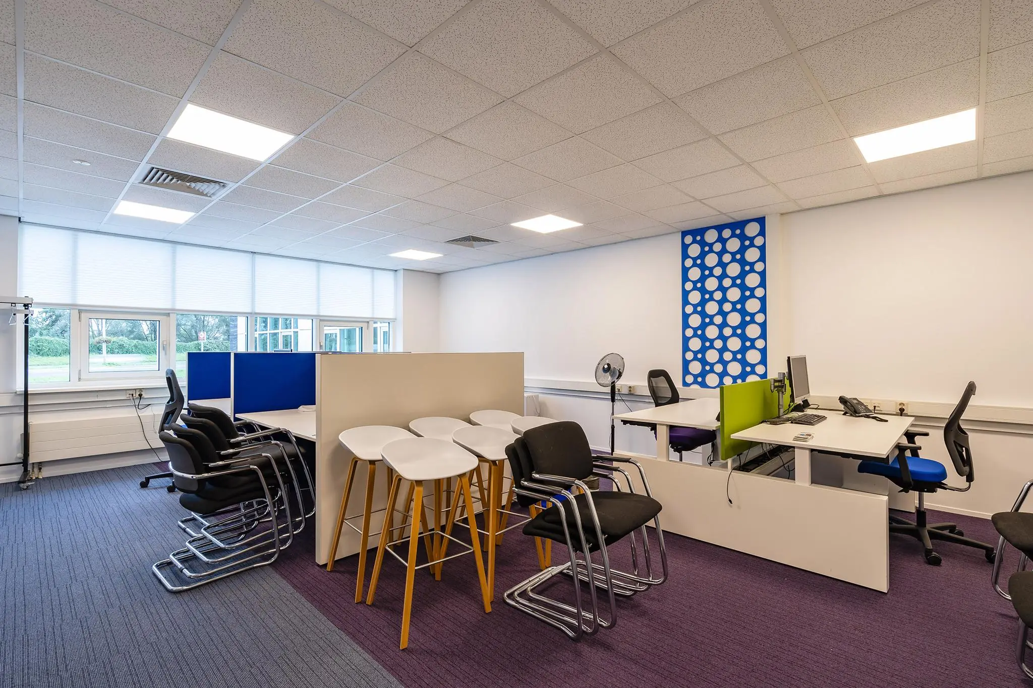 Moderne open kantoorruimte aan het Rhijnspoor met bureaus, bureaustoelen, gestapelde stoelen en hoge krukken.