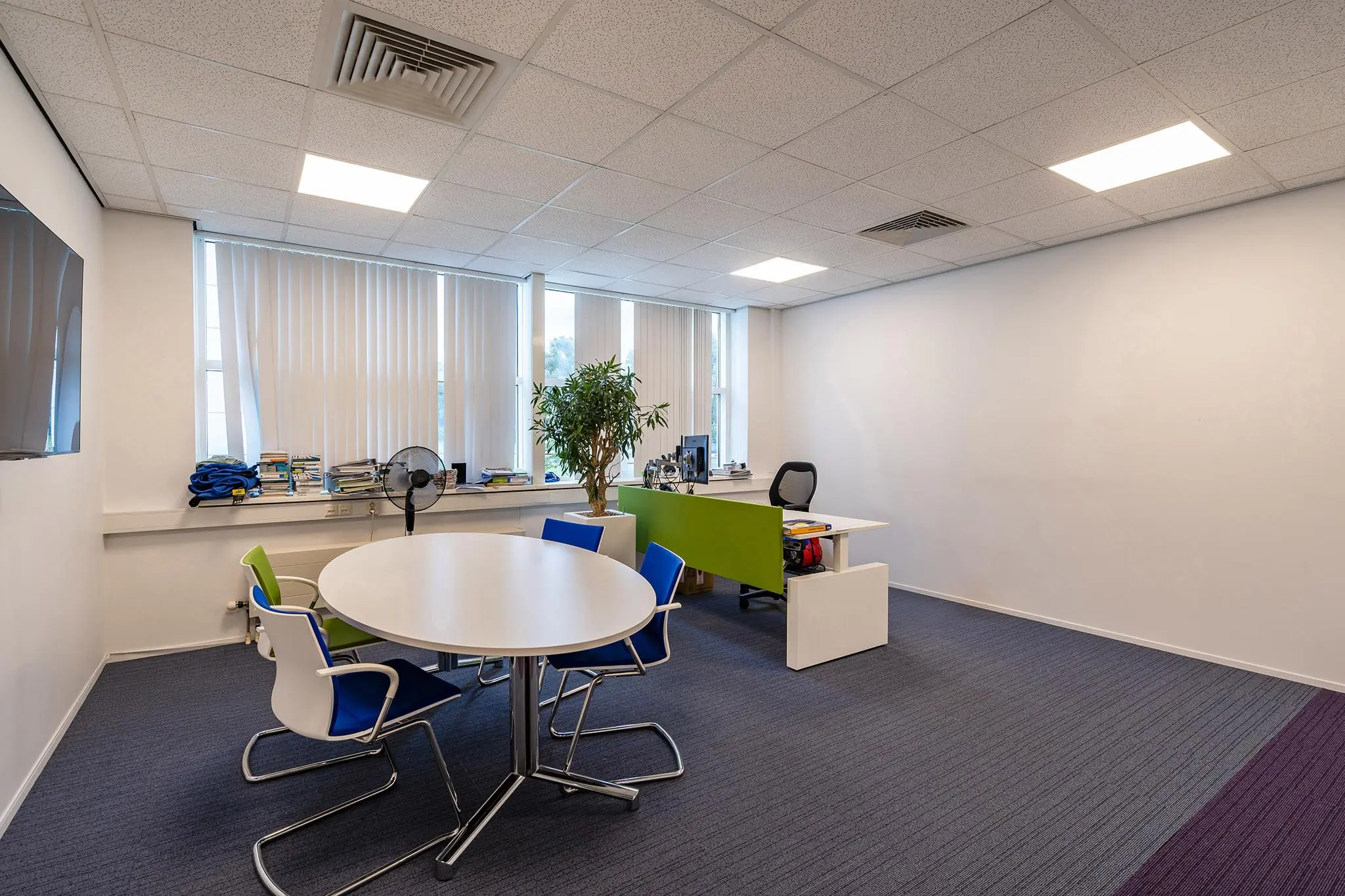 Modern kantoor met een bureau, vergadertafel, stoelen en grote ramen met verticale jaloezieën aan het Rhijnspoor.