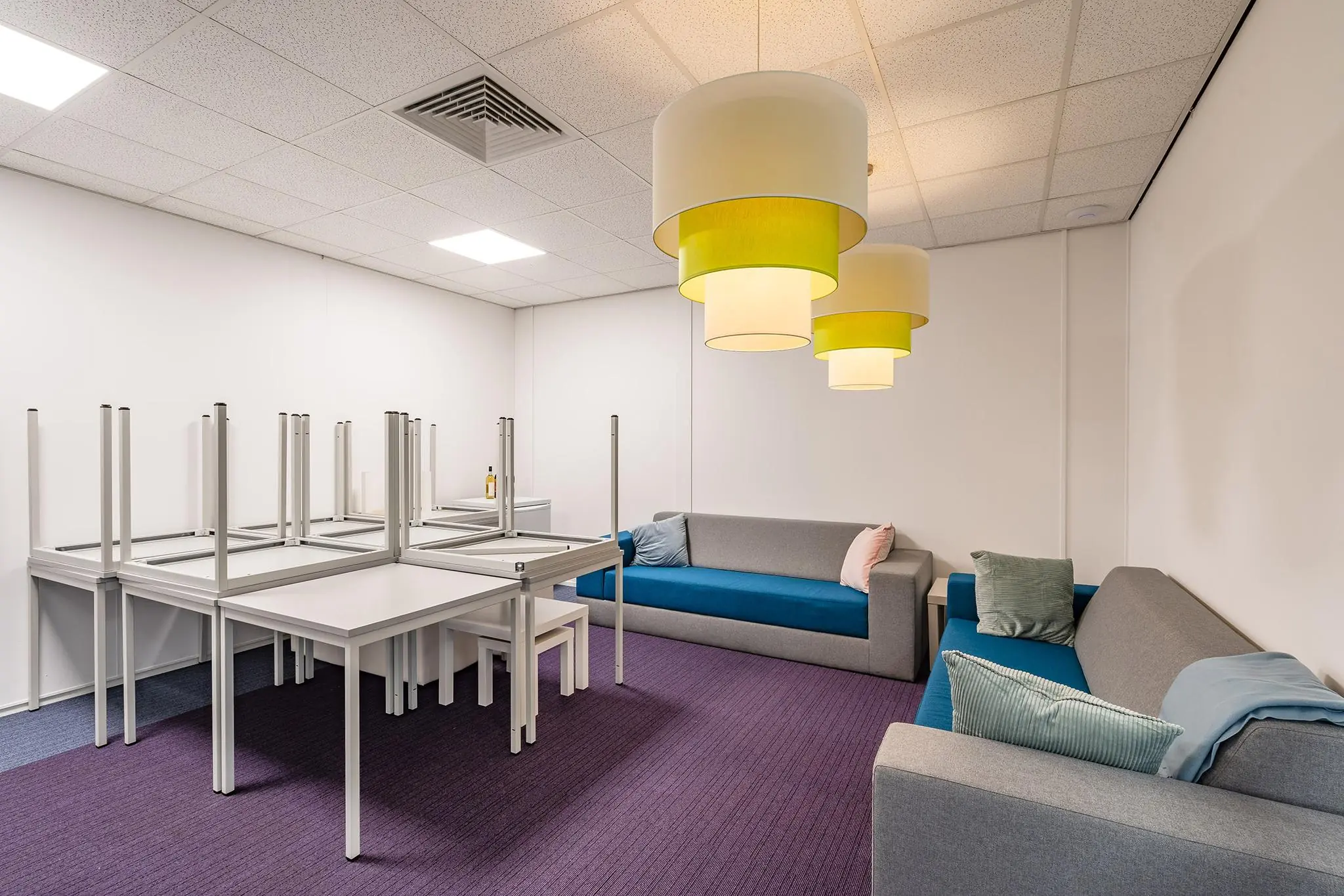 Wacht- of loungeruimte in kantoorpand Rhijnspoor met opgestapelde tafels, paarse vloerbedekking en moderne zitbanken.