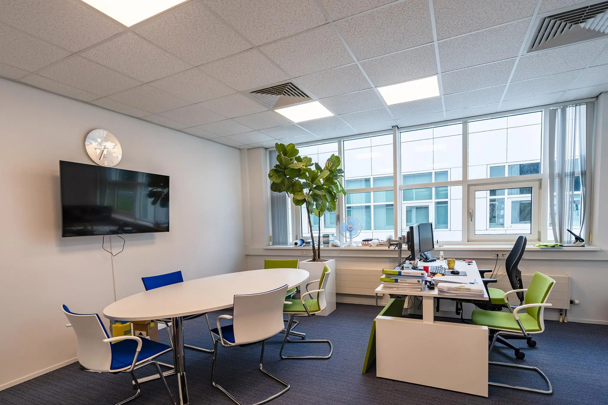 Moderne kantoorruimte aan het Rhijnspoor met werkplekken, vergadertafel, grote ramen en een kamerplant.