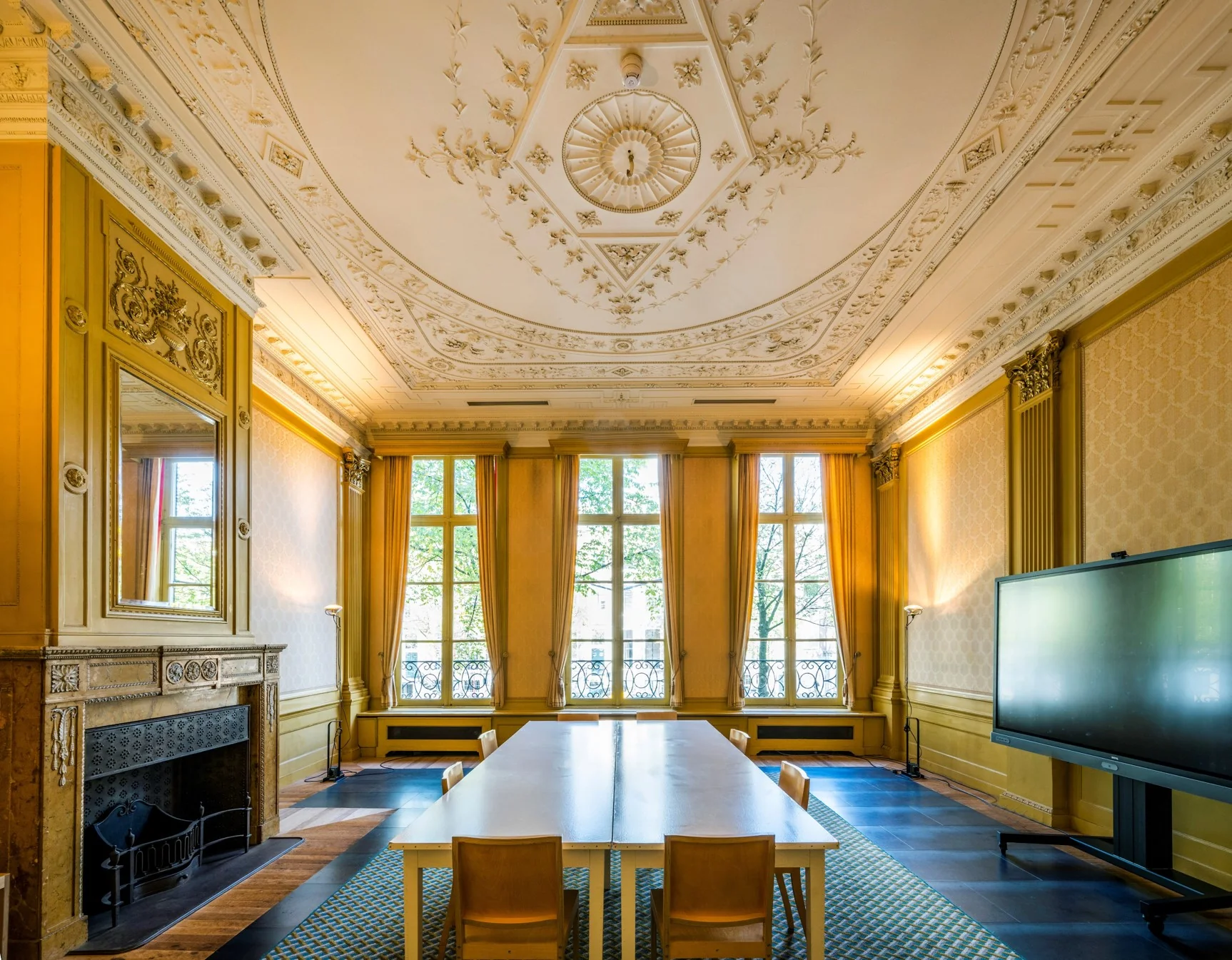Vergaderruimte aan de Herengracht met hoge ramen, sierplafond, open haard en een modern digitaal scherm.