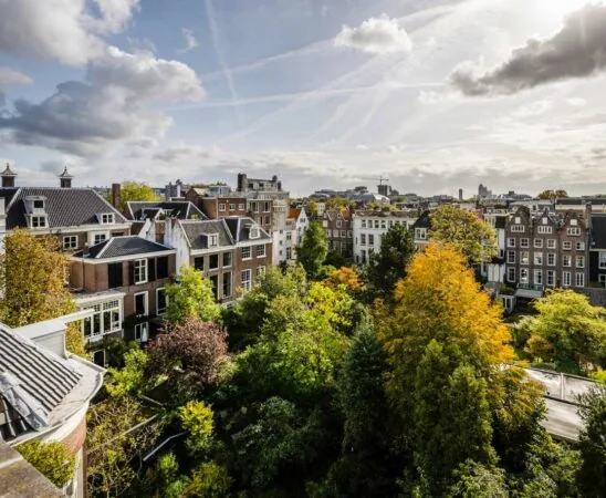 Uitzicht op klassieke herenhuizen aan de Herengracht in Amsterdam met een groene binnentuin en herfstkleuren.
