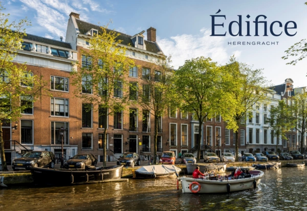 Zonnige gracht met varende boot langs historische panden aan de Herengracht in Amsterdam, met het logo van Édifice Herengracht.