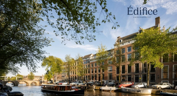Zicht op klassieke grachtenpanden aan de Herengracht in Amsterdam met een boot op de voorgrond en het logo van Édifice Herengracht rechtsboven.