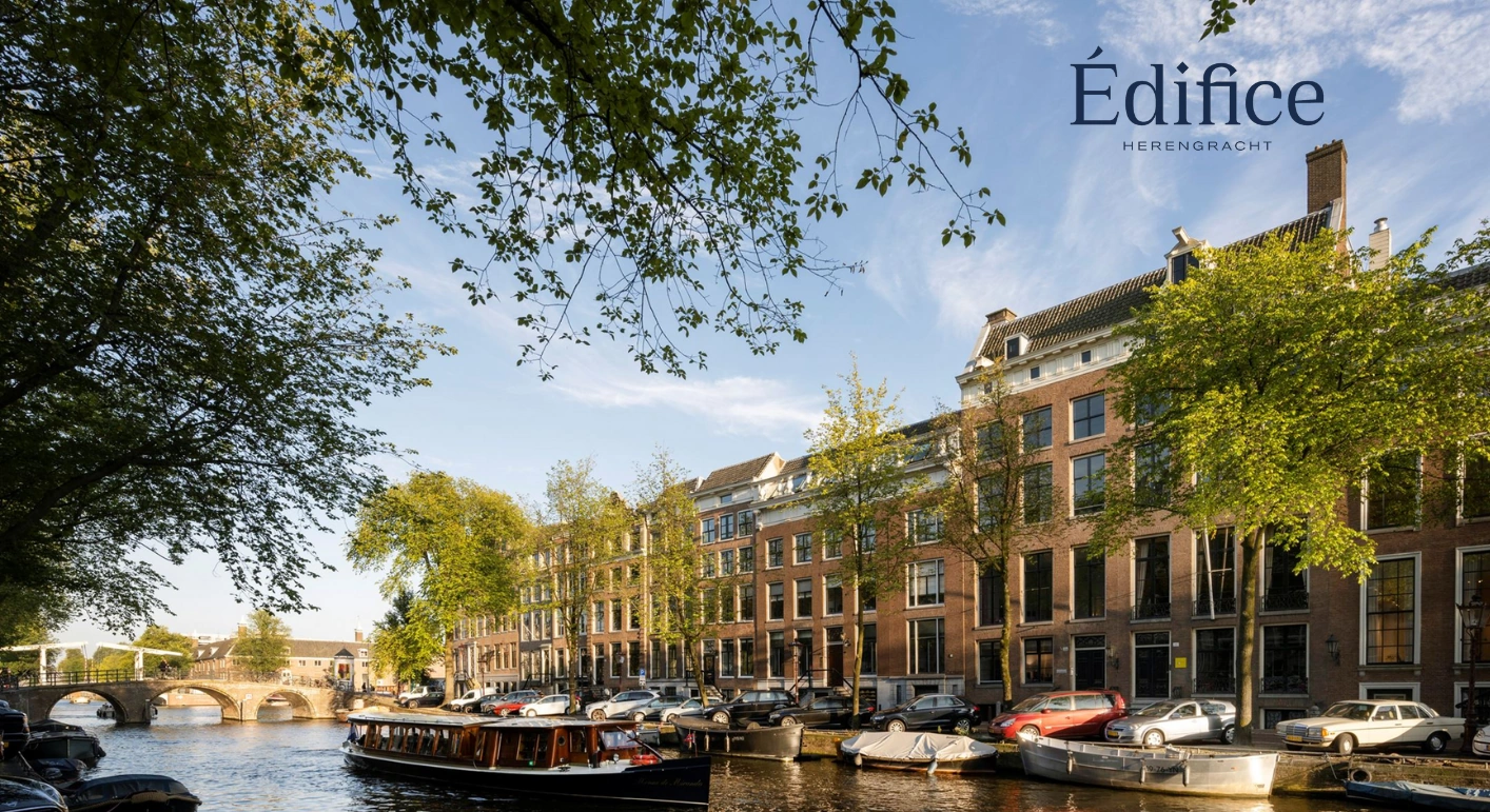 Zicht op klassieke grachtenpanden aan de Herengracht in Amsterdam met een boot op de voorgrond en het logo van Édifice Herengracht rechtsboven.