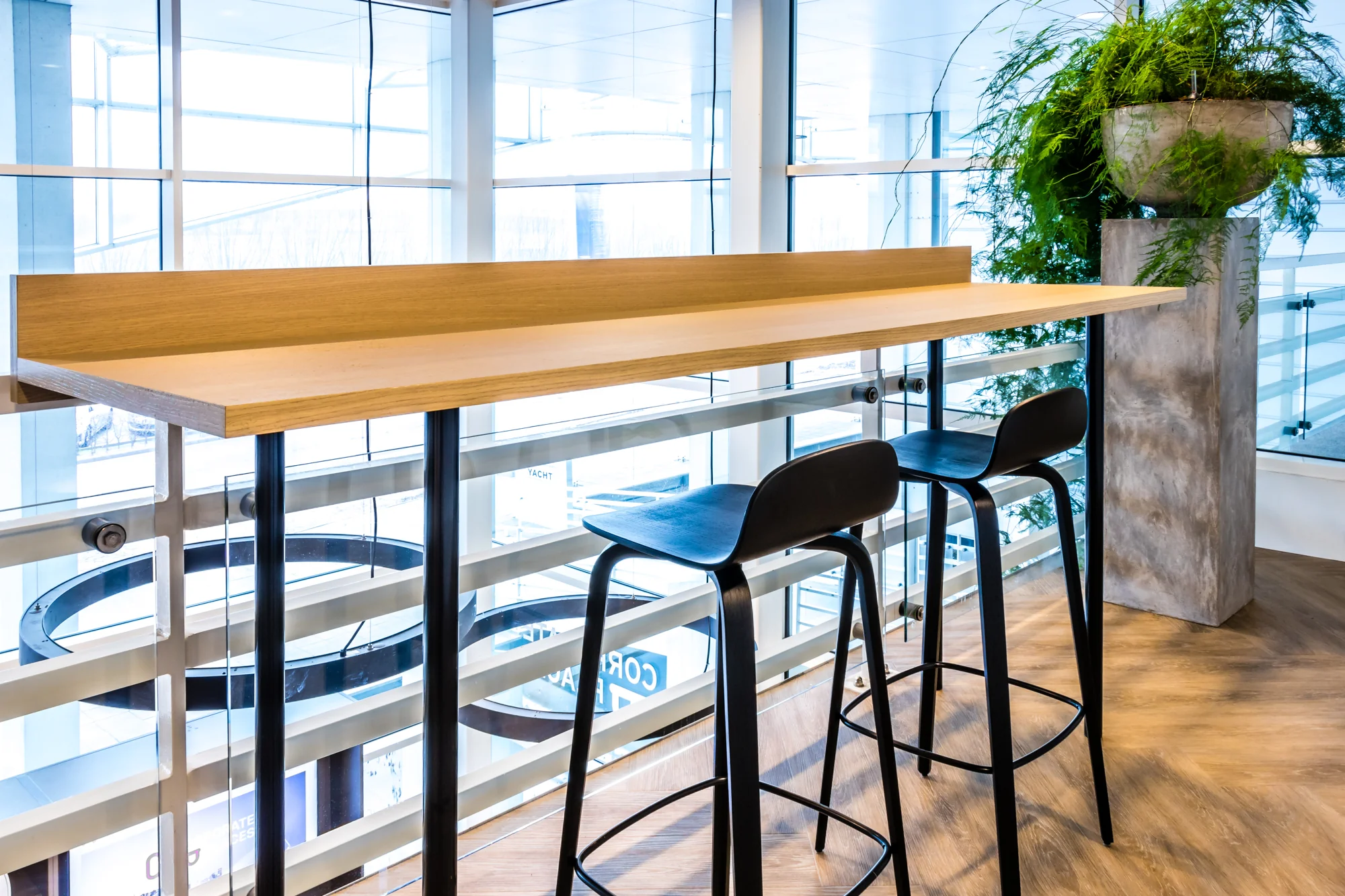 Hoge houten tafel met twee zwarte barkrukken bij het raam in een modern kantoor aan de Reactorweg.