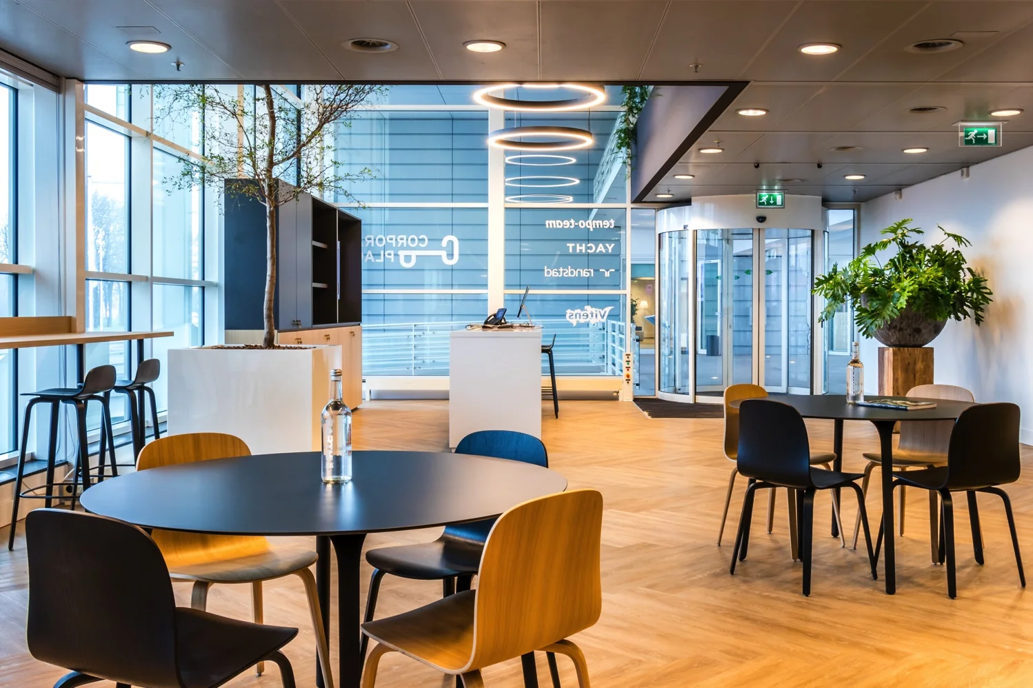 Moderne ontvangstruimte aan de Reactorweg met ronde tafels, designstoelen, planten en grote ramen.