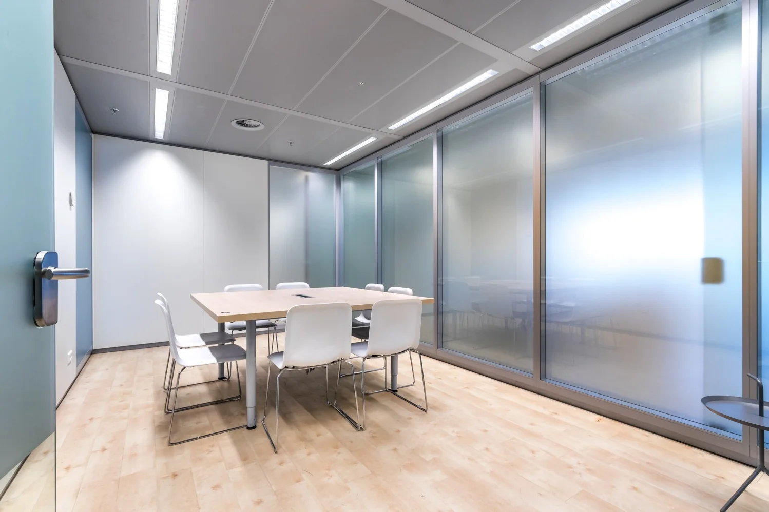 Vergaderruimte aan de Reactorweg met een houten tafel, zes witte stoelen en glazen wanden met matglas.