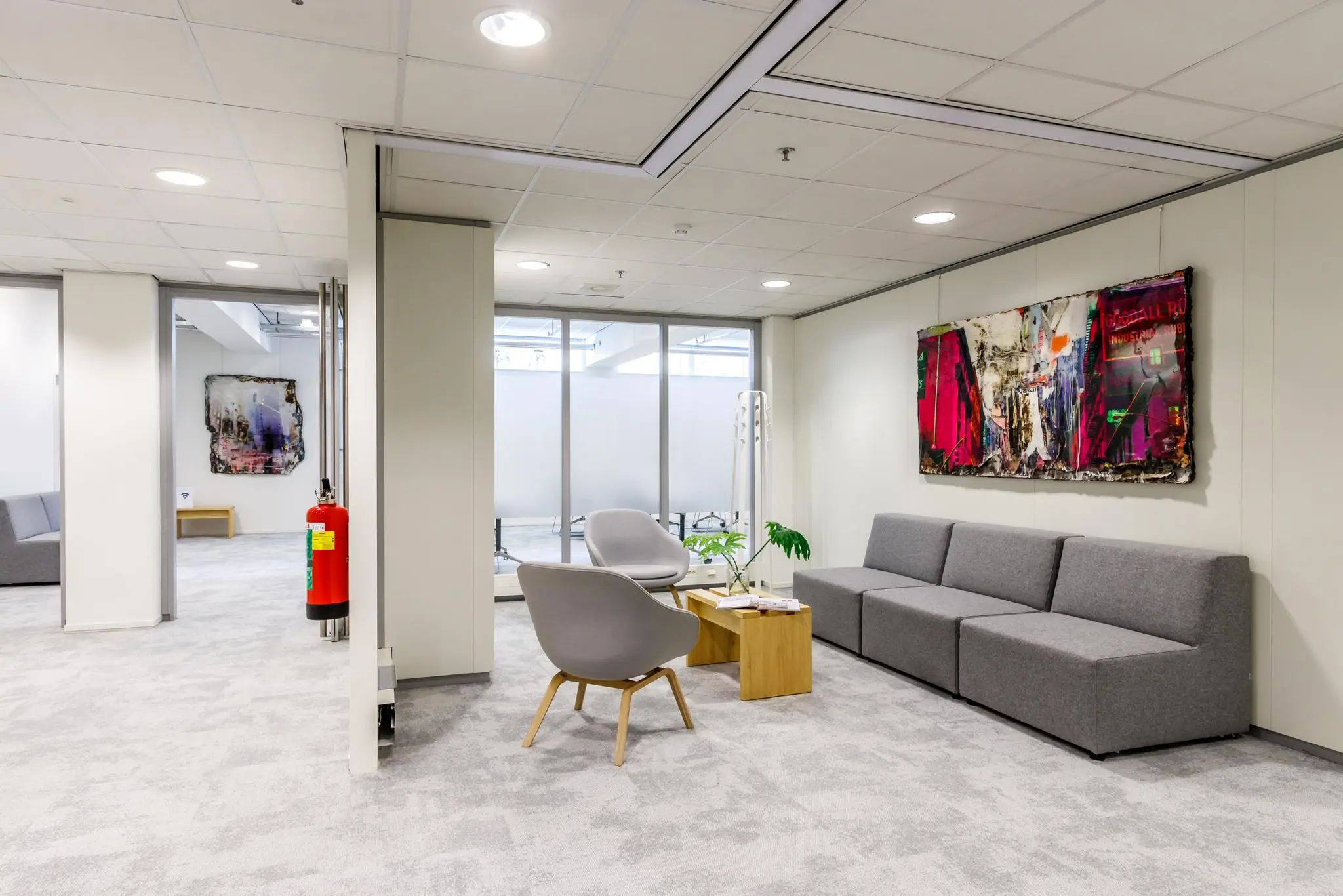 Moderne wachtruimte aan de Reactorweg met grijze zitmeubels, een houten tafel en kleurrijke kunst aan de muur.