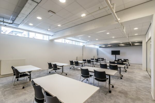 Moderne, licht ingerichte les- of vergaderruimte aan de Reactorweg met meerdere tafels, stoelen en een flatscreen.