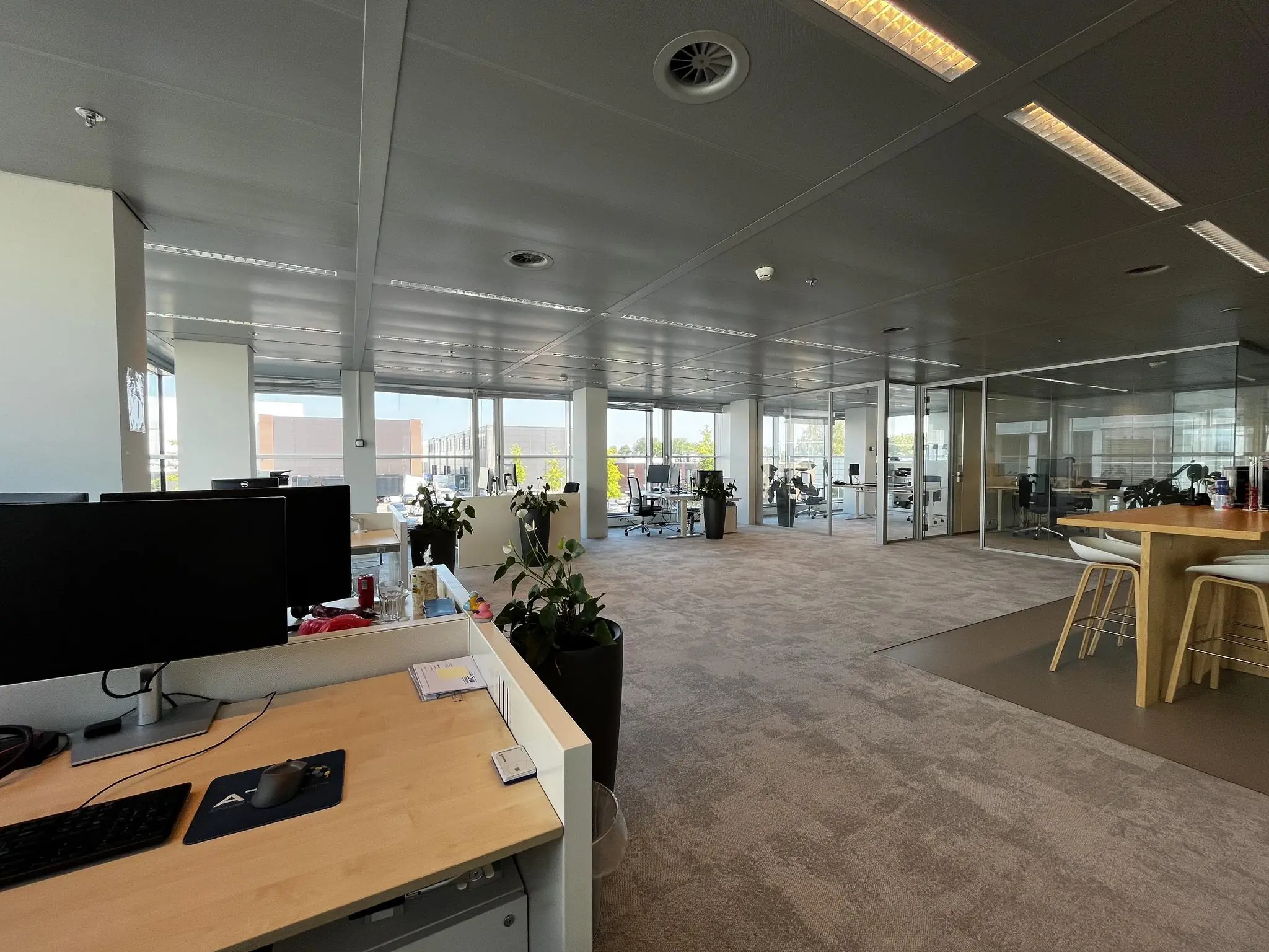 Modern kantoorinterieur aan de Reactorweg met open werkplekken, glazen vergaderruimtes en een hoge tafel met barkrukken.