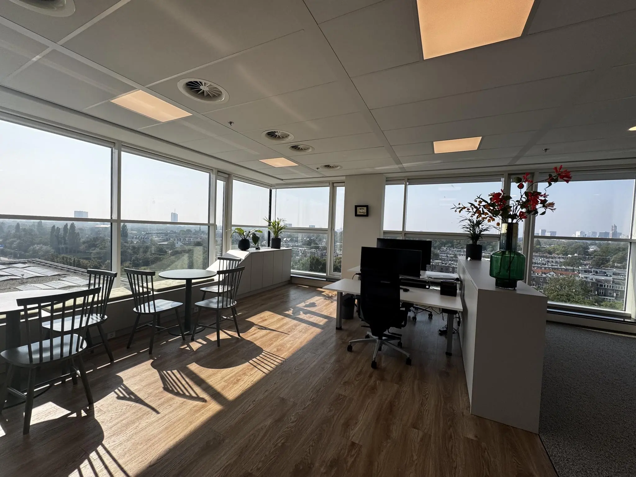 Modern hoekkantoor aan de Newtonlaan met grote ramen, een bureau, zitgedeelte en uitzicht over de stad.