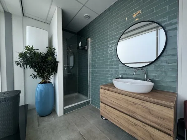 Moderne badkamer op Newtonlaan met houten wastafelmeubel, ovale spiegel en groene wandtegels.