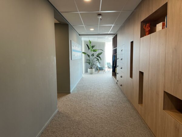 Moderne kantoorhal aan de Newtonlaan met houten kastenwand, planten en zithoek in de verte.