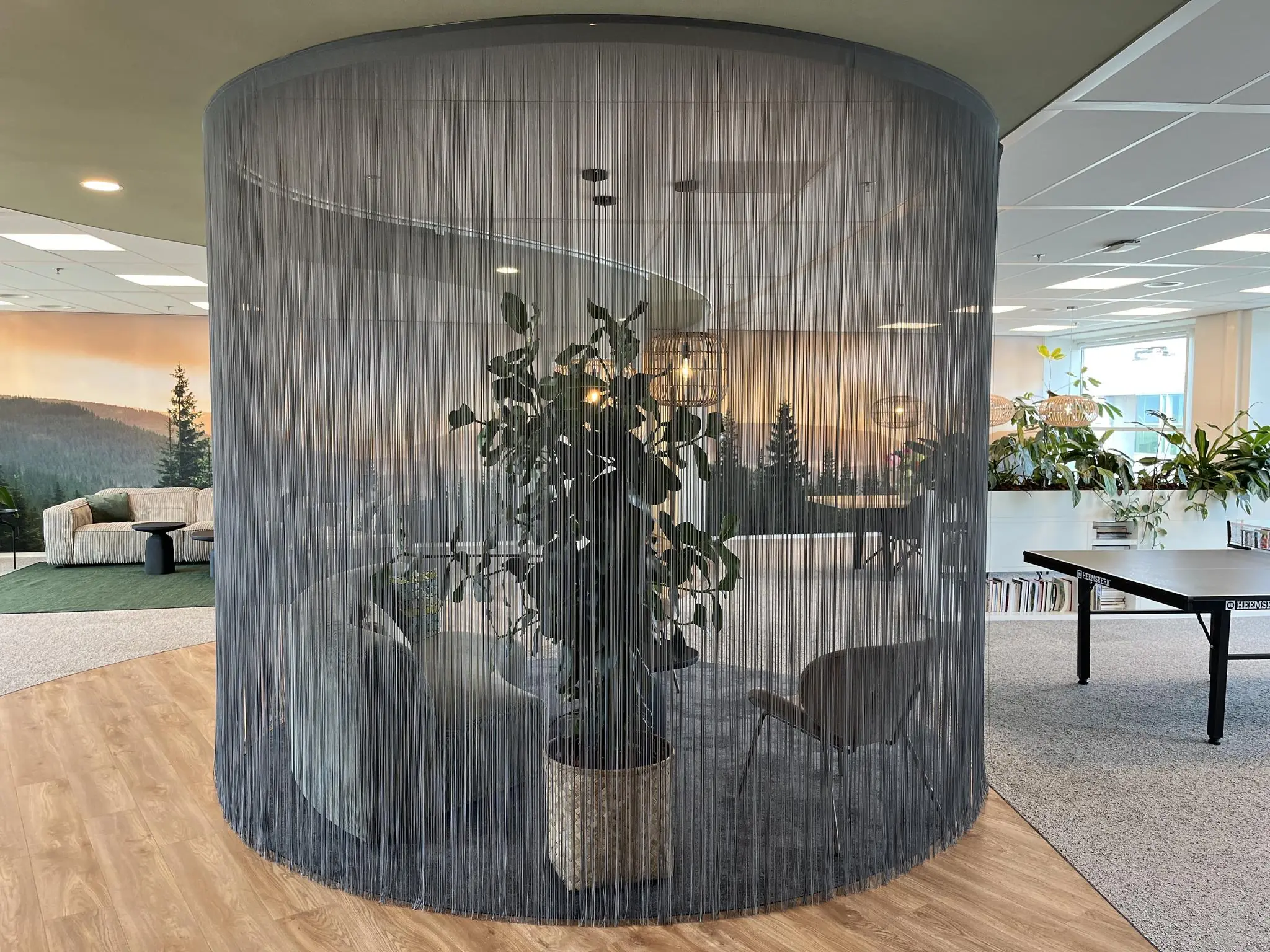 Moderne kantoorruimte aan de Newtonlaan met een ronde zithoek omringd door een gordijn van koorden, planten en een tafeltennistafel op de achtergrond.