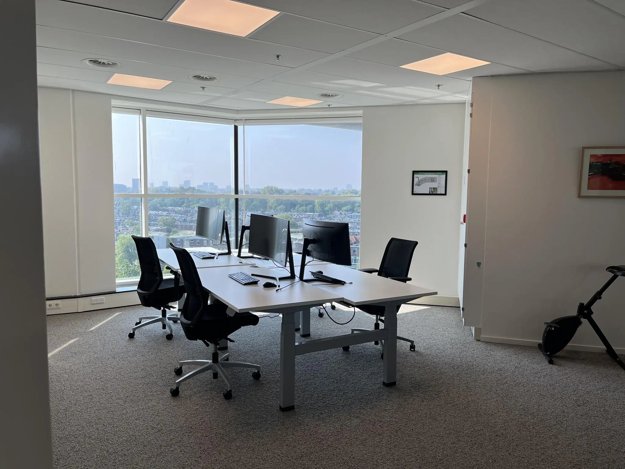 Modern kantoor met vier bureaustoelen en computerschermen, gelegen aan de Newtonlaan met uitzicht over de stad.