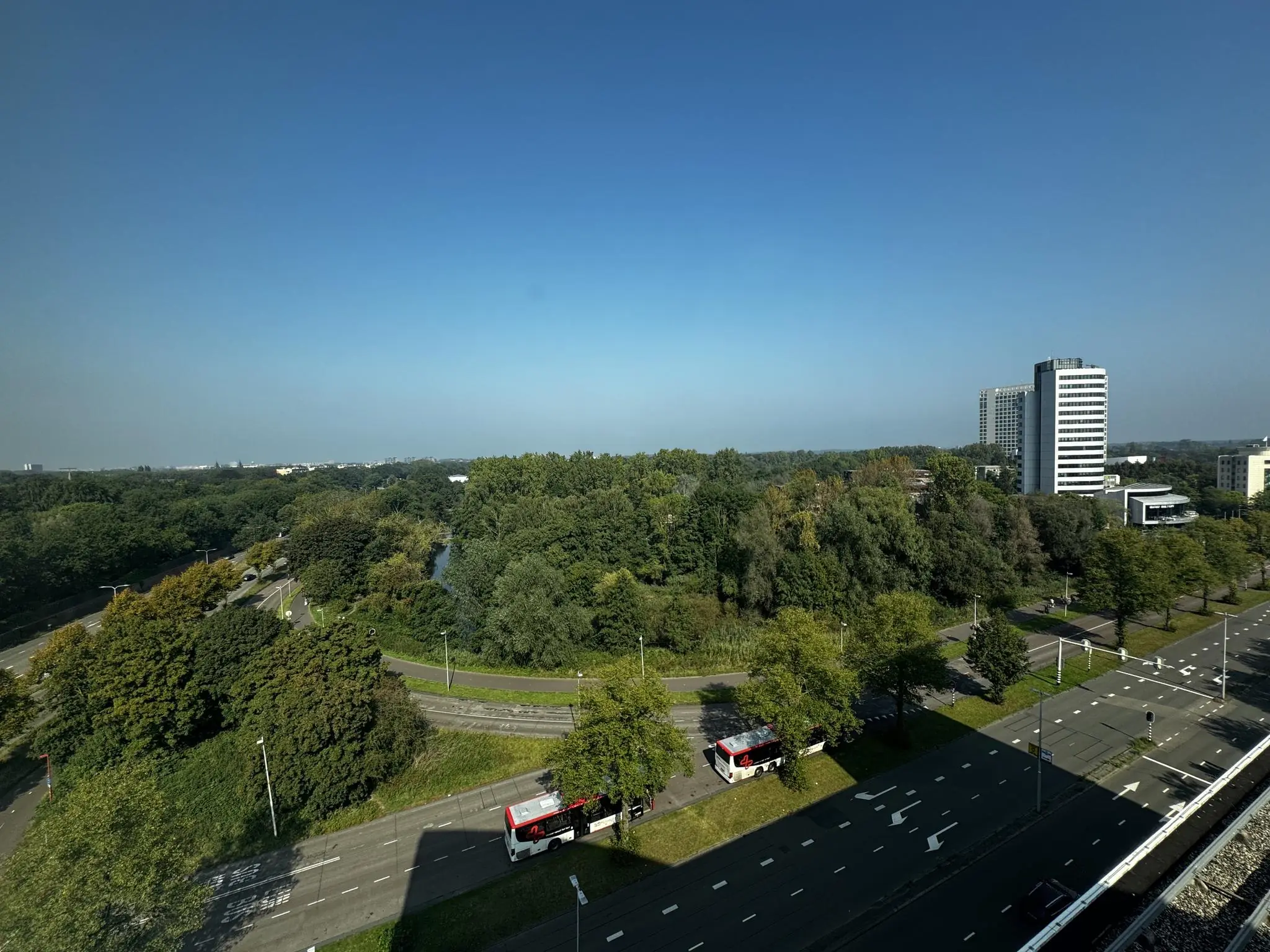 Uitzicht op Newtonlaan in Utrecht met kantoorgebouwen, een groene omgeving en een blauwe lucht.