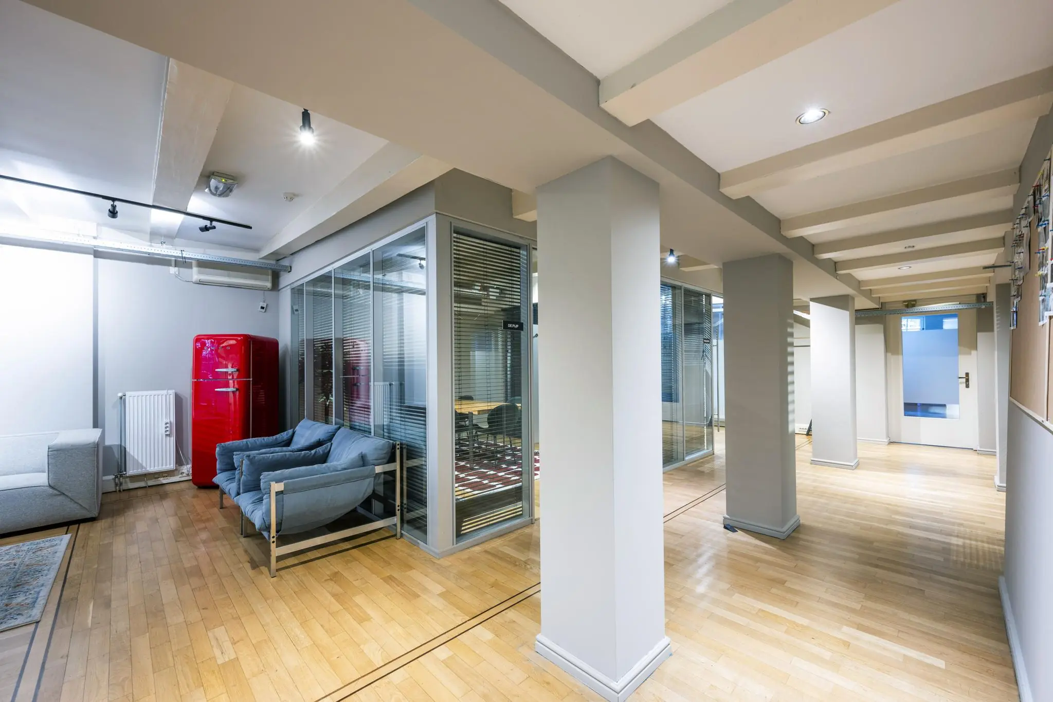 Modern kantoorinterieur aan de Herengracht met glazen vergaderruimtes, houten vloer en een opvallende rode retro koelkast.