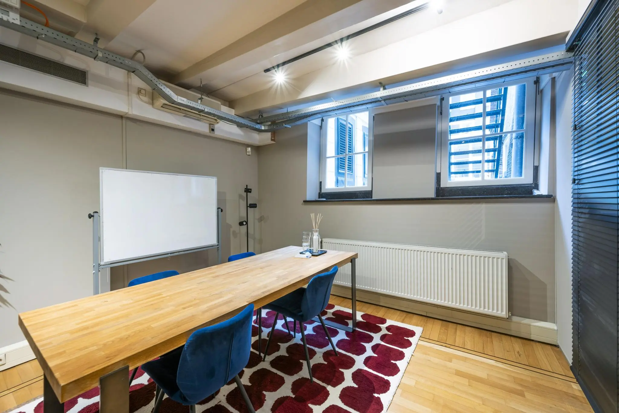 Vergaderruimte aan de Herengracht met houten tafel, blauwe stoelen, whiteboard en rood-wit vloerkleed.