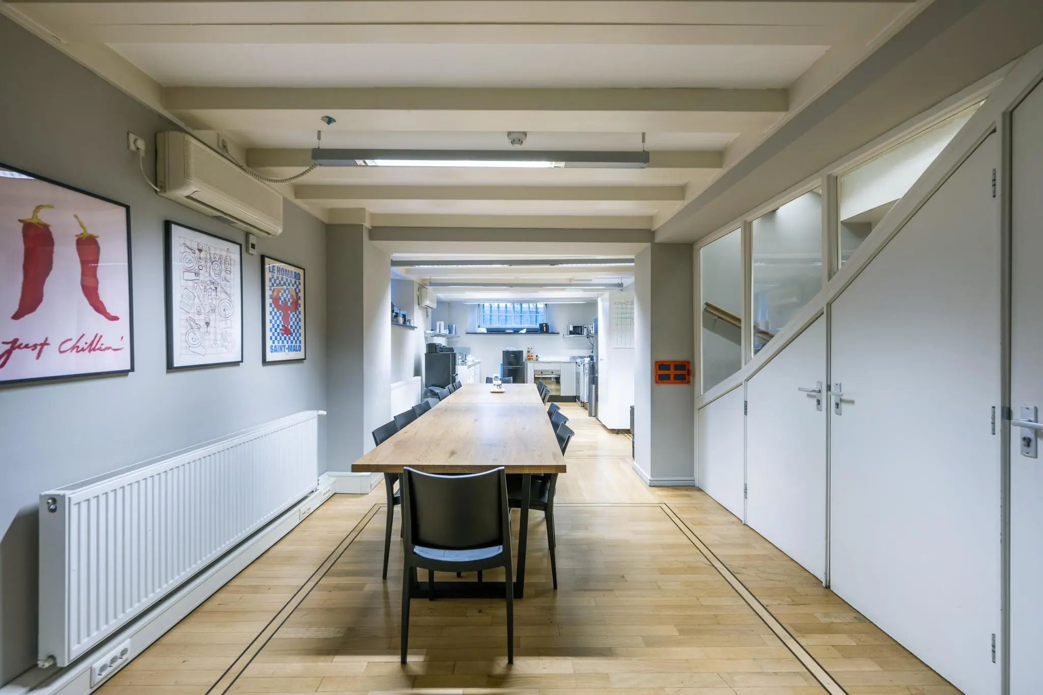 Moderne vergaderruimte aan de Herengracht met een lange houten tafel, zwarte stoelen en zicht op een open keuken.