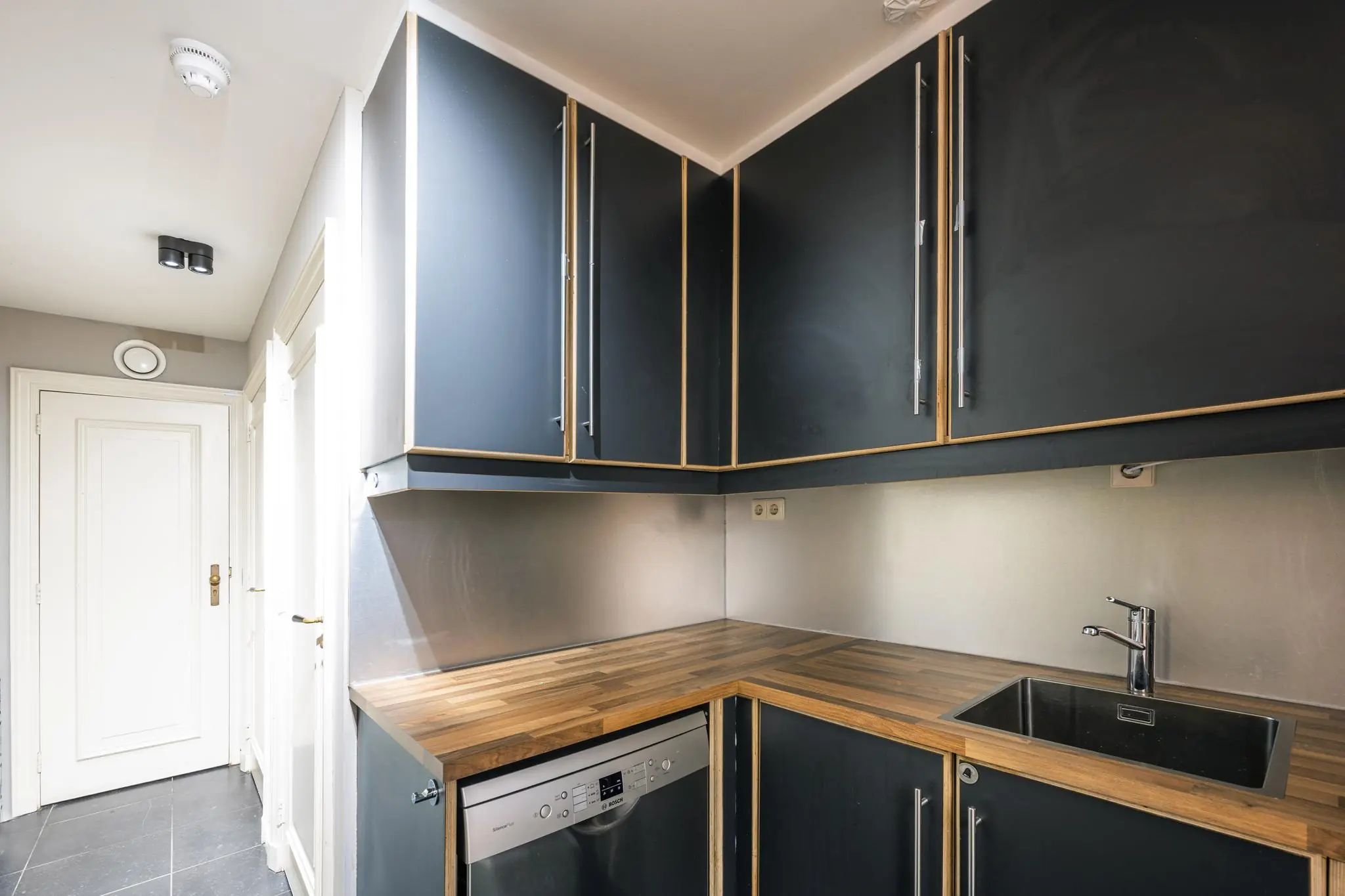Moderne hoekkeuken in Herengracht-appartement met donkerblauwe kasten, houten werkblad en roestvrijstalen wasbak.