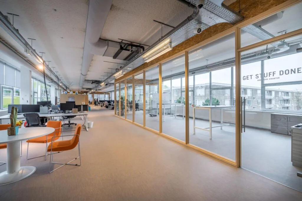 Modern kantoorinterieur aan de Helmholtzstraat met open werkplekken, glazen vergaderruimtes en de tekst "Get Stuff Done" op het raam.