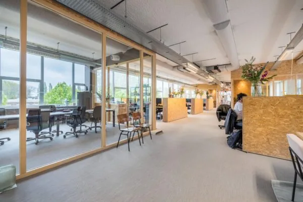 Modern kantoorinterieur aan de Helmholtzstraat met houten werkplekken, glazen vergaderruimte en grote ramen met uitzicht op groen.