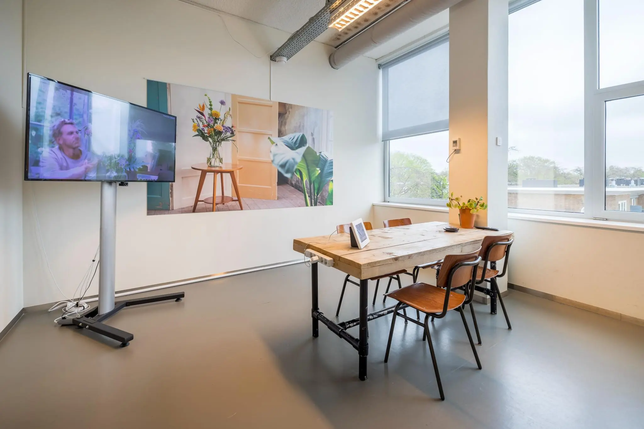 Vergaderruimte met houten tafel, vier stoelen, een flatscreen op standaard en grote ramen aan de Helmholtzstraat.
