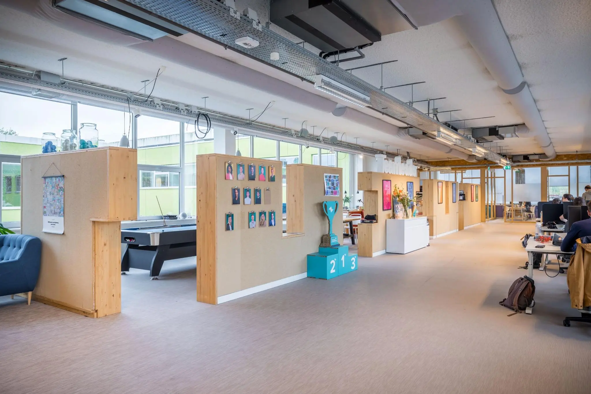 Moderne en kleurrijke kantoorruimte aan de Helmholtzstraat met open werkplekken, spelvoorzieningen en persoonlijke medewerkersfoto’s aan de wand.