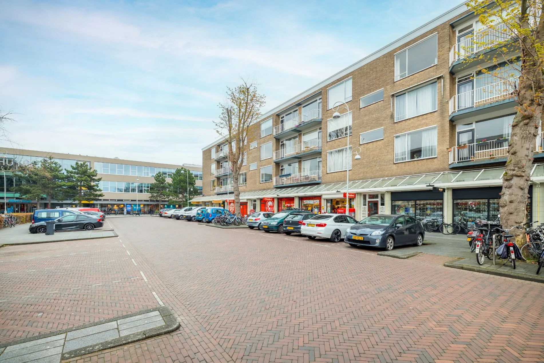 Winkelpand met bovenwoningen en geparkeerde auto's aan de Helmholtzstraat in een woonwijk.