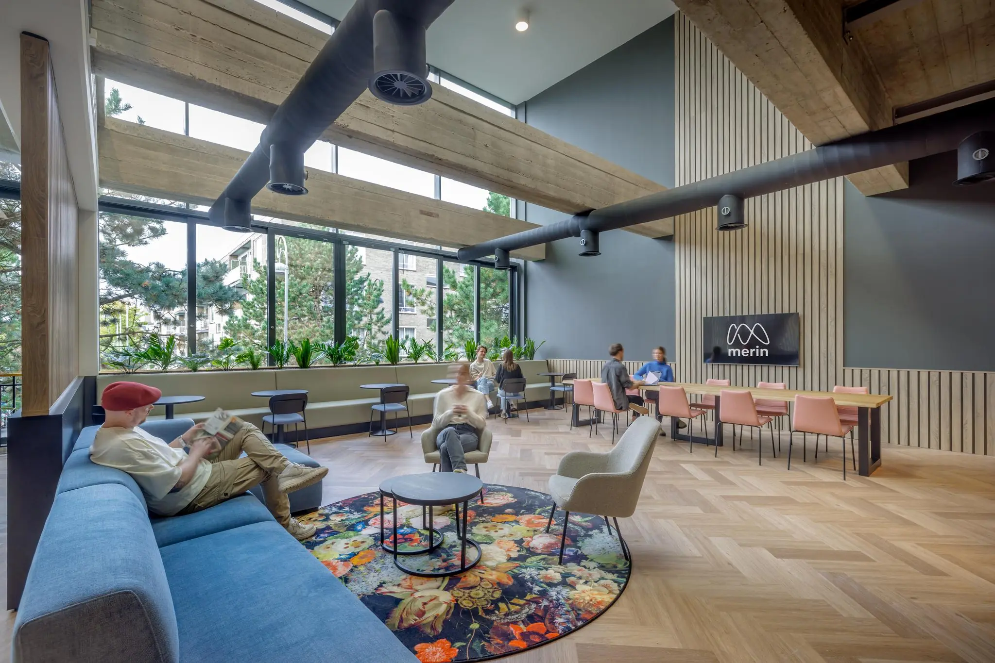 Moderne, lichtovergoten loungeruimte aan de Helmholtzstraat met zitgedeelte, vergadertafel en Merin-logo op de muur.