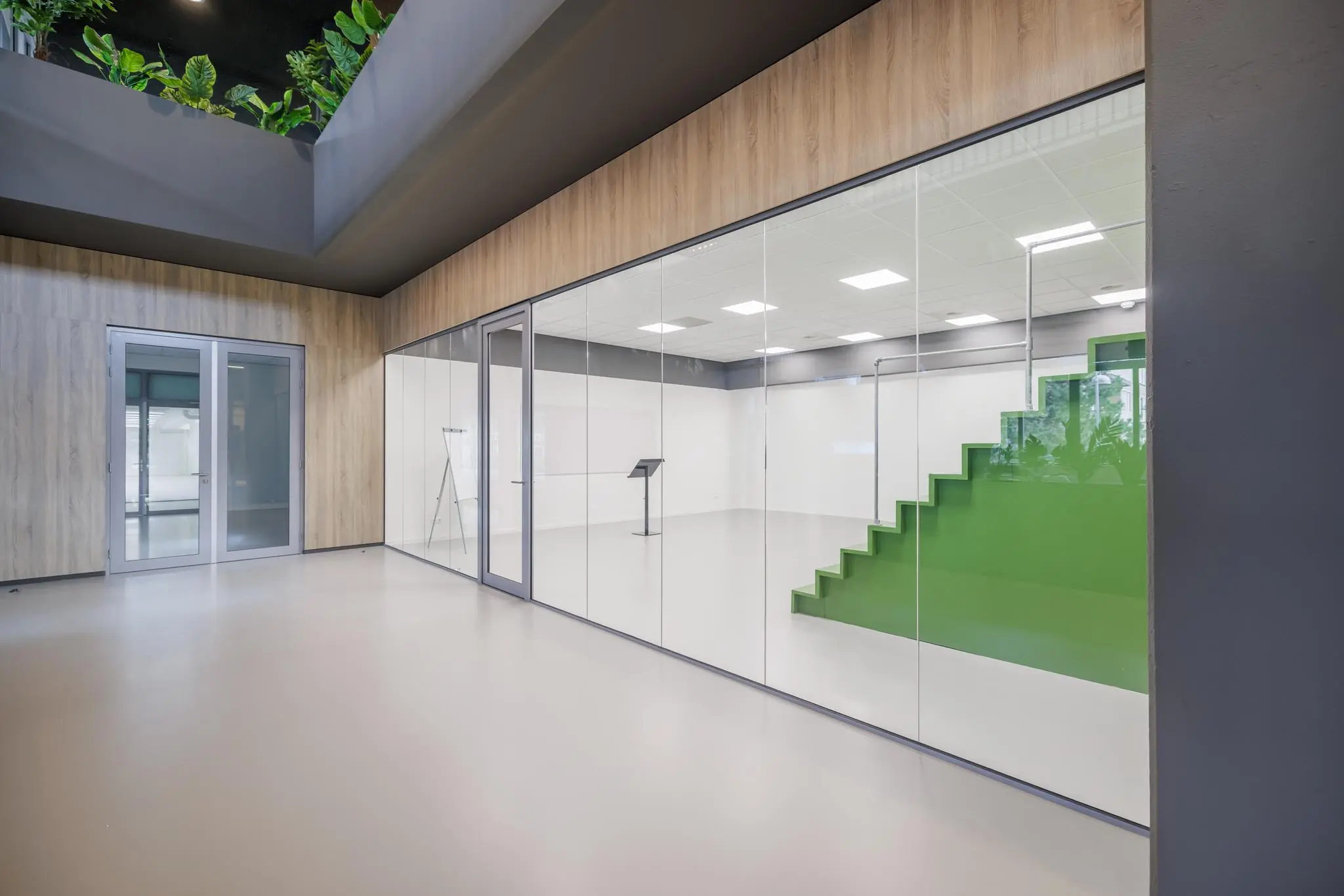 Moderne vergaderruimte aan de Helmholtzstraat met glazen wanden en een groene tribune in een strak afgewerkt interieur.