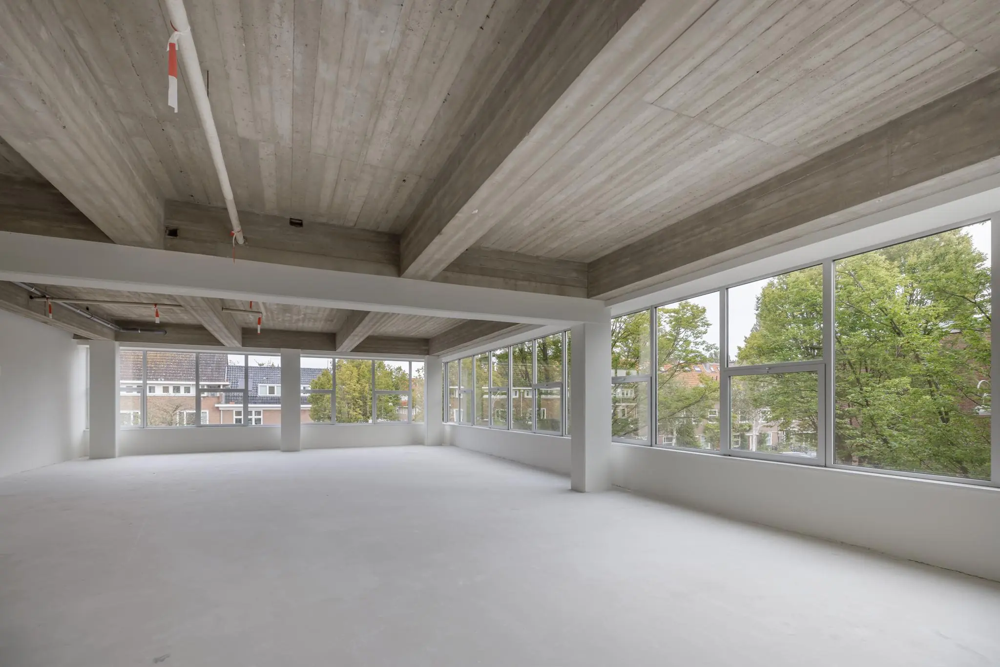 Licht en ruim leeg kantoorpand met betonnen plafond en grote ramen aan de Helmholtzstraat.