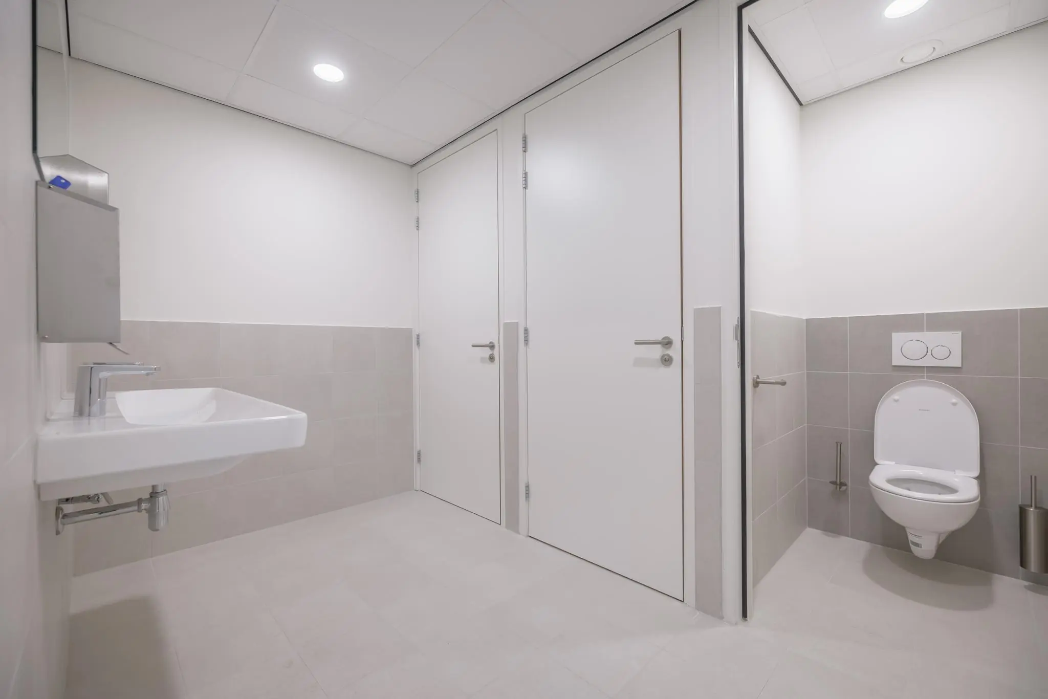 Moderne, licht betegelde toiletruimte in een gebouw aan de Helmholtzstraat met wasbak, toilet en afgesloten cabines.