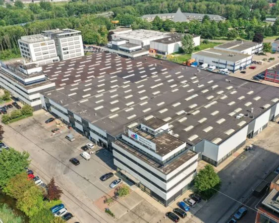 Luchtfoto van een groot industrieel pand met de naam "Media Onwijze" op het dak, omringd door kantoren, parkeerplaatsen en groen.