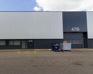 Vooraanzicht van een bedrijfsgebouw met de ingangen 47A en 47B, afvalcontainers en een "NP" (niet parkeren) zone op de stoep.