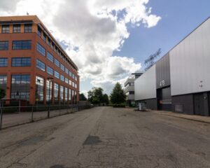 Bedrijventerrein met een rood bakstenen kantoorgebouw links en een grijs industriegebouw met het nummer 47B rechts onder een deels bewolkte lucht.