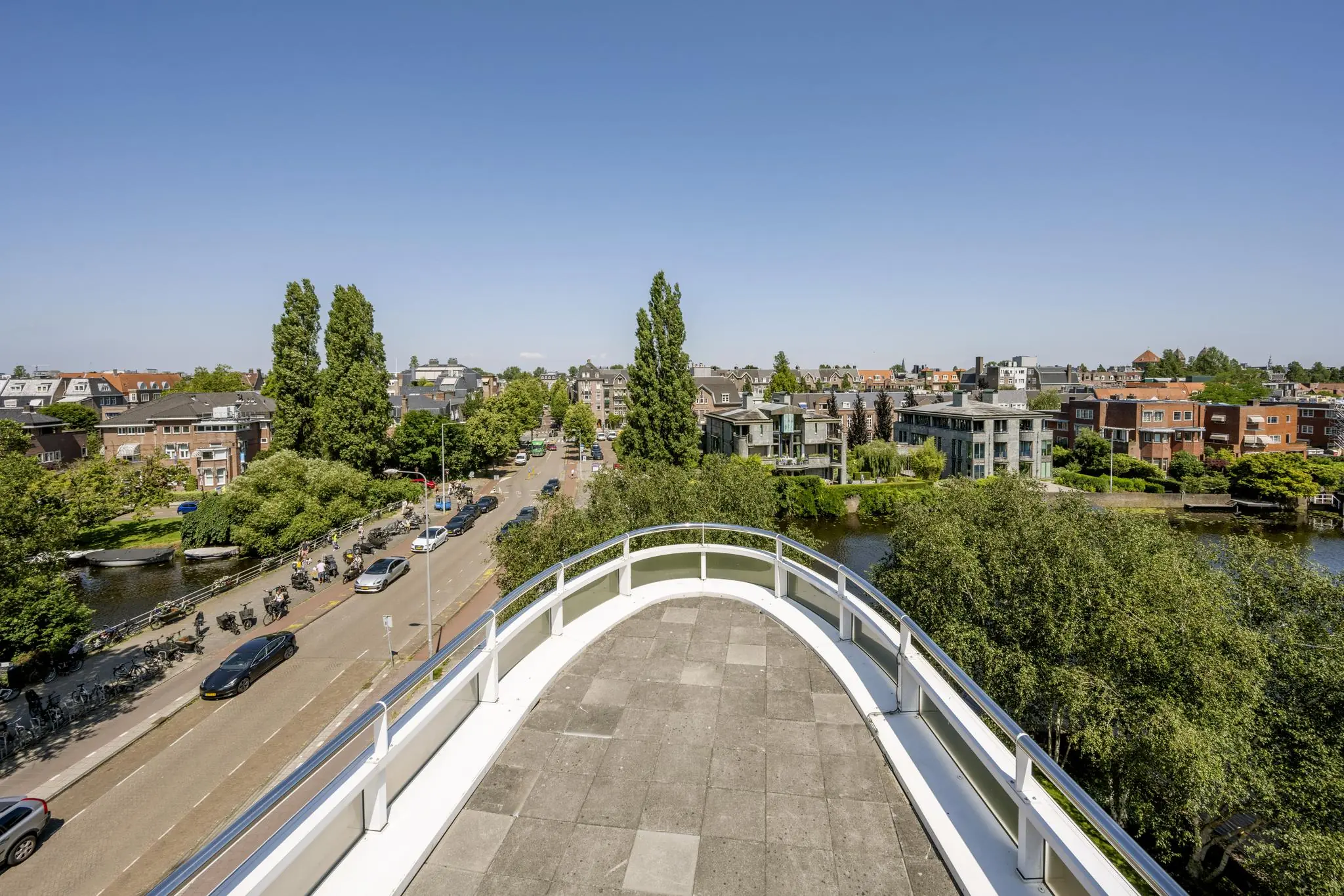 Uitzicht vanaf een dakterras op de Apollolaan in Amsterdam met omliggende woningen, water en groen.