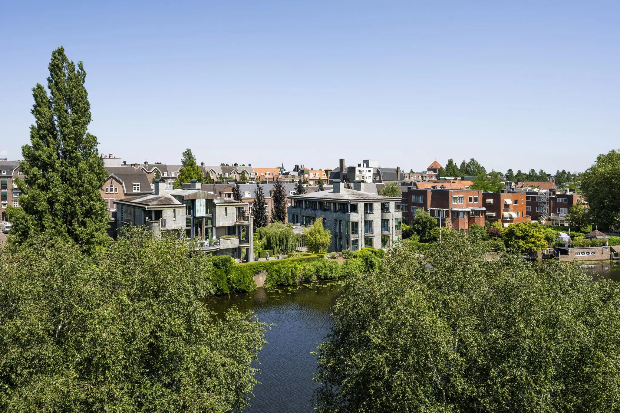 Uitzicht op moderne en klassieke woningen aan de Apollolaan in Amsterdam, gelegen langs een waterpartij met omliggend groen.