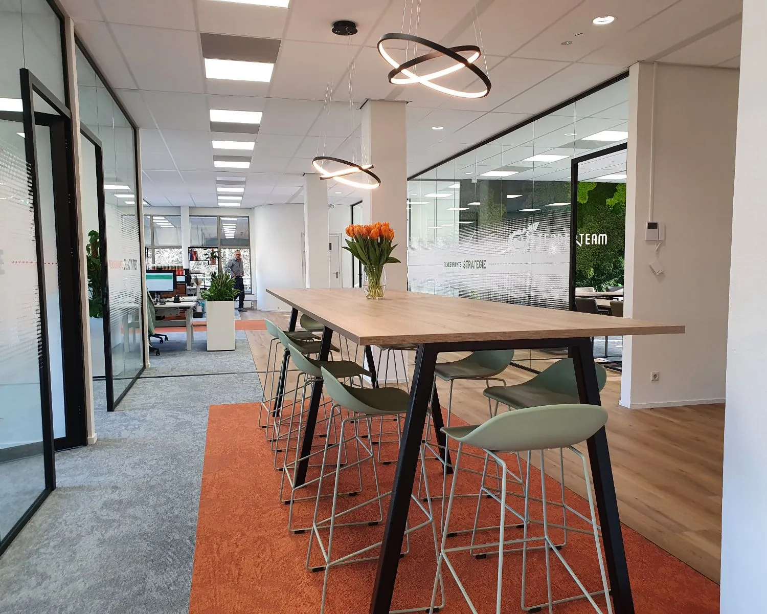 Moderne kantoorruimte met een hoge vergadertafel, designkrukken en een vaas oranje tulpen als centerpiece.