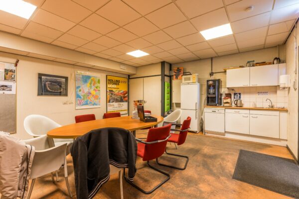 Vergader- en kantineruimte met ovale tafel, keukenblok, koffieautomaat en posters aan de muur, waaronder één van de Rolling Stones Licks World Tour 2003.