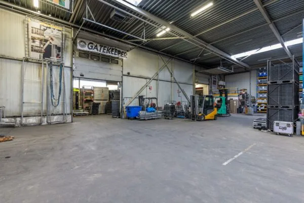 Magazijnruimte van Veldzigt met heftrucks, opslagrekken en materiaal bij de toegangspoort met het bord 'Gatekeeper'.