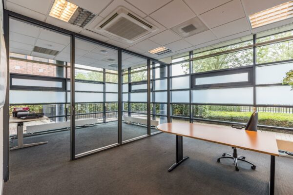 Modern en licht kantoor met glazen wanden, uitzicht op groen en een enkel bureau met bureaustoel.
