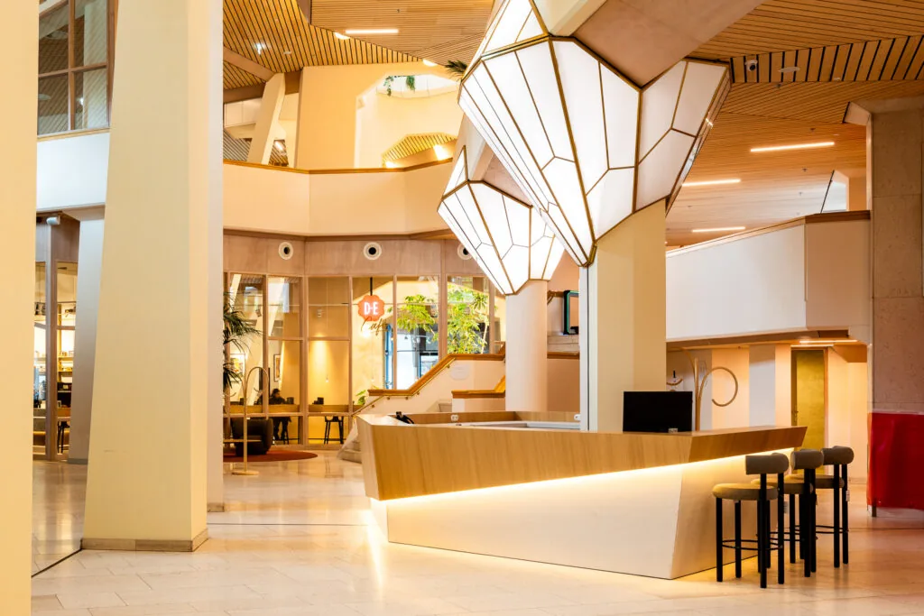 Modern interieur van het Zandkasteel met een centraal ontvangstbalie, opvallende lichtarmaturen en zicht op café DE.