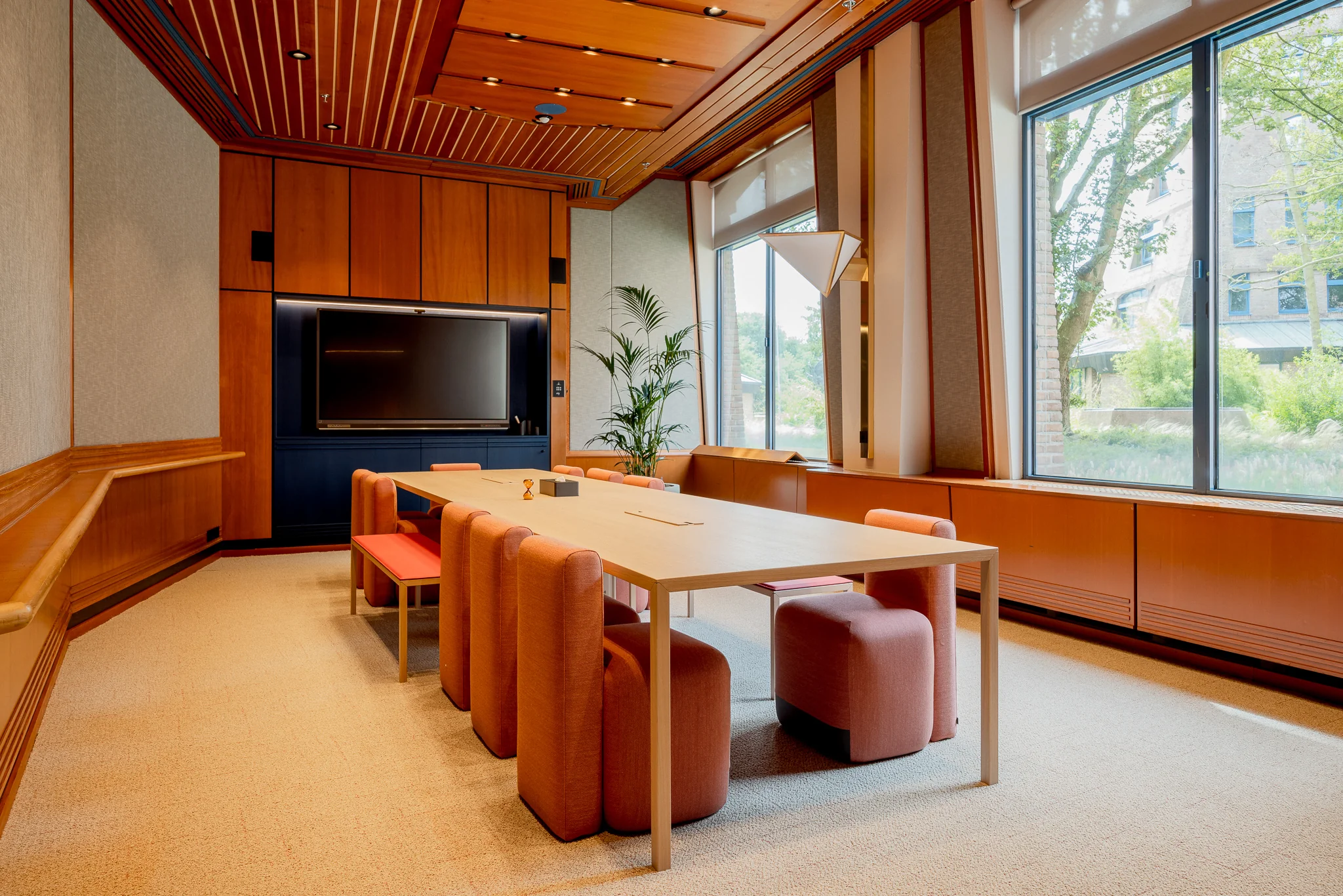 Vergaderruimte in het Zandkasteel met een lange tafel, oranje stoelen, houten interieur en grote ramen met uitzicht op groen.