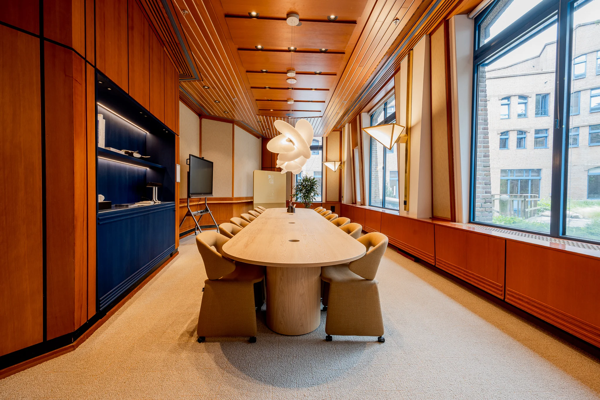 Vergaderruimte in Het Zandkasteel met houten wanden, ovale vergadertafel, designverlichting en grote ramen met uitzicht op een binnenplaats.